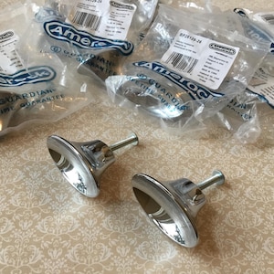 May include: A collection of polished chrome cabinet knobs, some still in their original packaging. The knobs have a flared, bell-shaped design with a long, cylindrical post. The packaging includes the Amerock logo and product information.