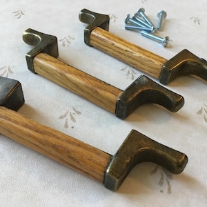 Könnte beinhalten: Drei Schrankgriffe mit einem hellen Holzmaserungszentrum und bronzefarbenen Metallenden. Die Griffe sind rechteckig mit einem gebogenen Griffdesign. Mehrere silberne Schrauben sind enthalten.