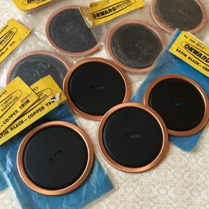 May include: A selection of black cabinet hardware backplates with copper trim. The backplates are circular, featuring a black centre and a copper-coloured rim. Several are in their original packaging, with yellow labels reading "ONWARD" and "SATIN BLACK - COPPER TRIM".