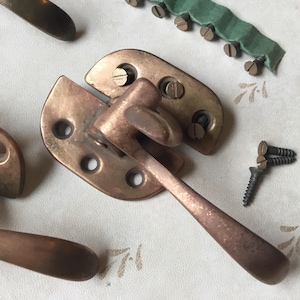 May include: Close-up of antique bronze hardware, including a latch with a handle, mounting plates, and screws. The metal has a weathered, aged appearance. A green fabric strip with small screws is also visible.