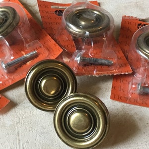 May include: Four brass cabinet knobs with a raised, concentric circle design. The knobs are packaged individually with screws.