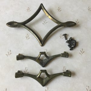 Puede incluir: Juego de herrajes antiguos en tono latón, que incluye un tirador en forma de diamante y dos tiradores más pequeños, junto con varios tornillos. El herraje tiene una estética vintage, adecuado para la restauración de muebles.