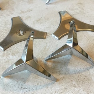 Pode incluir: Cinco pés de mobiliário de metal cromado com base triangular e três pontas. Os pés são projetados para serem fixados na parte inferior das pernas dos móveis.