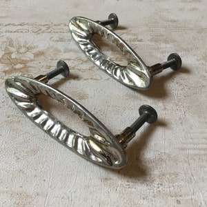 May include: Two silver oval cabinet pulls with a decorative, textured design. The pulls have a screw on each end for installation.