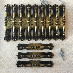 Peut inclure: Ensemble de poignées et de tirettes de meubles de style ancien. La quincaillerie présente une finition noire et dorée, avec des détails décoratifs. Comprend plusieurs poignées et tirettes, ainsi que des vis de montage.