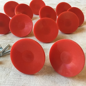 May include: Ten red plastic cabinet knobs with a slightly raised centre. The knobs are round and have a smooth, glossy finish.