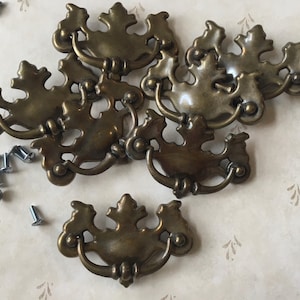 May include: Six antique brass cabinet knobs with ornate leaf designs. Each knob has a single hole for mounting.