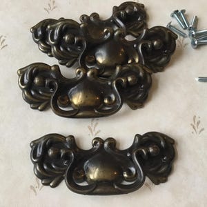May include: Four ornate, antique-style cabinet pulls with a brass finish. The pulls have a decorative, floral design and are in the shape of a half-circle.