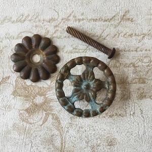 May include: Two antique brass drawer pulls with a floral design. One pull is round with a flower in the centre and the other is flower-shaped with a round centre.