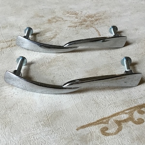 May include: Two silver cabinet door pulls with a curved, twisted design. The pulls have a brushed finish and are attached to the door with screws.