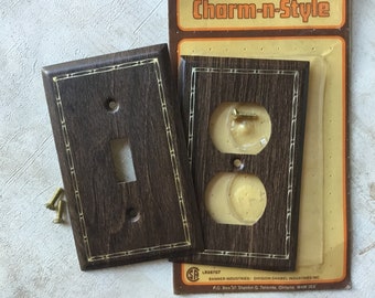 May include: Two vintage brown wood electrical outlet and switch covers with gold trim. The outlet cover has two holes and the switch cover has one. The packaging reads "Charm-n-Style".