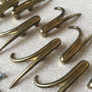 May include: A collection of antique brass drawer pulls and handles with a curved design. The hardware is a warm gold color, with a vintage aesthetic. Includes screws for installation.