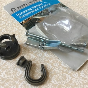 May include: A package of Handy Helper rotating hanger suspension hardware. The package includes a metal hook, a metal bracket, and screws. The package also includes a plastic piece. The hardware is a dark gray color.