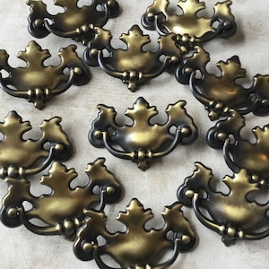 May include: Ten antique brass cabinet pulls with a leaf design. The pulls have a decorative, ornate design with a curved handle.