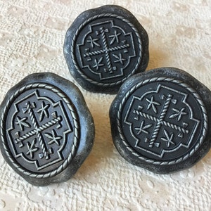 May include: Three black metal cabinet knobs with a silver finish. Each knob features a raised, intricate design of a cross with a rope border.