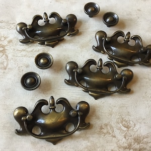 Peut inclure: Ensemble de quatre poignées de tiroir en laiton antique avec des motifs ornés. Les poignées ont un design décoratif et orné avec une poignée en boucle. Il y a aussi quatre boutons ronds assortis.