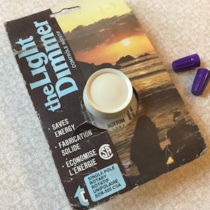 May include: A vintage light dimmer control with a cream-colored knob, on a brown and black package. The package has the text "the Light Dimmer" and "Saves Energy". Two purple wire connectors are also present.