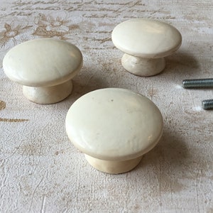 Puede incluir: Tres pomos de armario de cerámica de color crema con forma de hongo.