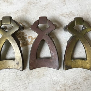 Op de afbeelding: Drie antieke messing kastdeurgrepen met een ingewikkeld geometrisch ontwerp. De grepen zijn in verschillende messingkleuren, waaronder goud, brons en koper.