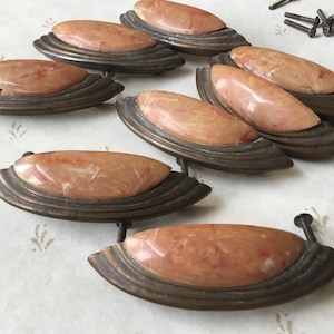 Op de afbeelding: Een set van tien antieke kastknoppen met een marmerachtig, perzikkleurig ontwerp. De knoppen zijn gemaakt van metaal met een messing afwerking en hebben een decoratieve, gegolfde rand.