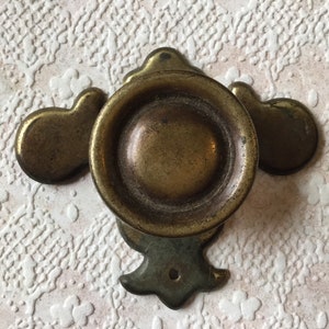 Puede incluir: Un pomo de puerta de latón con un diseño decorativo. El pomo es redondo y tiene un centro elevado. El pomo está unido a una placa decorativa con un diseño floral.