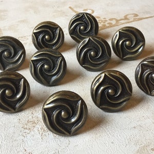 May include: Ten antique brass cabinet knobs with a swirling design. Each knob has a raised centre dot and a triangular shape.