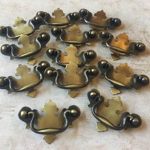 May include: A group of 15 antique brass cabinet pulls with a decorative, ornate design. Each pull has a curved handle and a decorative backplate.