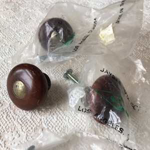 May include: Three brown wooden cabinet knobs with gold accents. The knobs are packaged in plastic bags with the text "Jaybee Mfg. Co. Los Angeles, CA 90054 Made in Taiwan" printed on the bags.