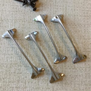 Peut inclure: Quatre poignées de tiroir argentées au design moderne et élégant. Chaque poignée est longue et étroite, avec une extrémité pointue et une poignée légèrement incurvée.