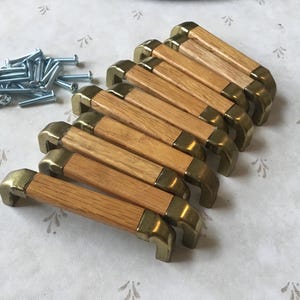 May include: A set of ten wooden cabinet knobs with gold metal accents. The knobs are arranged in a row, with the gold accents facing the viewer. The knobs are made of a light-coloured wood, and the gold accents are shiny.