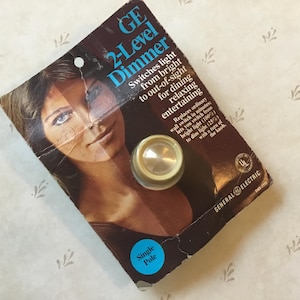 May include: A vintage GE 2-Level Dimmer light switch package with a single pole design. The package features a woman's face and a close-up of the dimmer switch. The text on the package reads "GE 2-Level Dimmer" and "Switches light from bright to out-of-sight for dining relaxing entertaining".