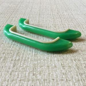 Op de afbeelding: Een paar vintage groene poppenschoenen met een witte rand. De schoenen zijn felgroen van kleur en hebben een afgerond teenontwerp. De schoenen zijn gemaakt van een glad, glanzend materiaal.