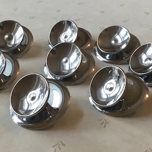 Peut inclure: Huit plats ronds et peu profonds de couleur argentée avec une surface réfléchissante. Les plats sont disposés en demi-cercle sur une surface blanche.