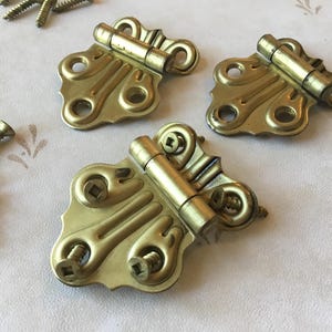 Puede incluir: Tres bisagras doradas en forma de mariposa con detalles decorativos. Cada bisagra tiene dos tornillos.