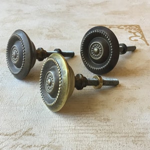May include: Three antique-style cabinet knobs with a circular design. The knobs are made of metal and have a dark brown finish. The knobs have a raised, circular design in the center and a beaded edge.