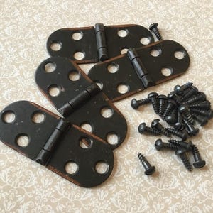 May include: A collection of black metal hinges and screws. The hinges are oval-shaped with rounded ends and three holes on each side. The screws are small and dark, and the background has a floral pattern.