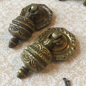 Op de afbeelding: Twee antieke messing lade-knoppen met sierlijke, bolvormige knoppen en achthoekige achterplaten. De knoppen hebben een vintage uitstraling, met gedetailleerde gravures en een warme, verouderde afwerking. Inclusief schroeven.