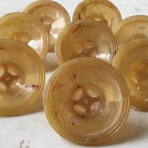 Op de afbeelding: Negen vintage, ronde, doorschijnende, amberkleurige decoratieve kommen met een swirl-patroon. Elke kom heeft een klein, rond, verhoogd ontwerp in het midden.