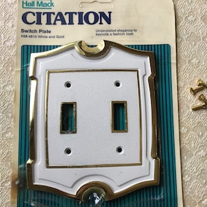 May include: White and gold double light switch plate with a decorative border. The plate is labeled "CITATION" and "HM-4810 White and Gold".