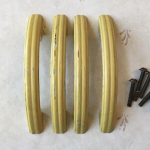 Op de afbeelding: Vier vintage gele metalen kastdeurgrepen met een geribbeld ontwerp.