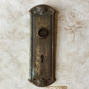 Puede incluir: Placa de puerta de latón antiguo con una cerradura y un pomo redondo. La placa tiene un diseño decorativo alrededor de los bordes.