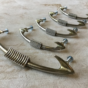 May include: Five silver-toned metal cabinet pulls shaped like a fish hook with a decorative ribbed design.