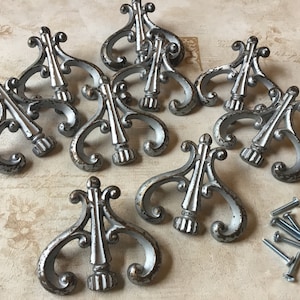 Puede incluir: Diez tiradores de cajón de metal plateado con diseños de volutas ornamentados. Los tiradores tienen un acabado desgastado y vienen con tornillos.