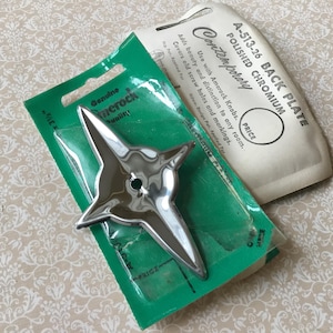 May include: A polished chrome starburst-shaped cabinet hardware piece on a green backing card. The card reads "Genuine Amerock" and "PRICE". A vintage back plate package is also present, labeled "Contemporary".