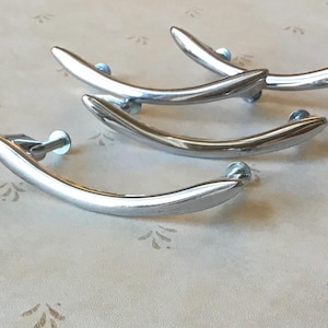 May include: Four silver-toned cabinet door pulls with a curved design. The pulls have a simple, modern style.