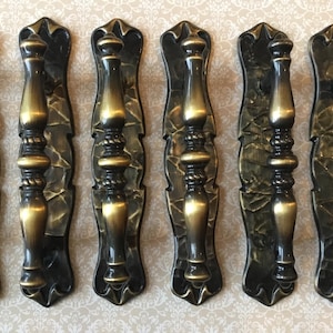 May include: Six antique-style door handles with a dark bronze finish and gold accents. The handles have a decorative, ornate design with a vertical grip and a textured backplate. Ideal for vintage home decor.