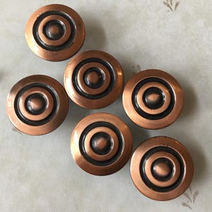 May include: Six copper cabinet knobs with a concentric circle design. The knobs have a dark brown finish and are arranged in a semi-circle.