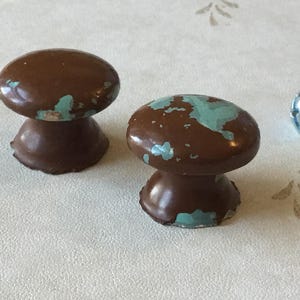 Może przedstawiać: Dwa brązowe ceramiczne pokrętła do szafki z wzorem rozpryskującej się farby w kolorze turkusowym.