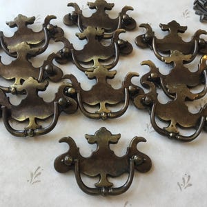 May include: A set of ten antique brass cabinet knobs with ornate designs. The knobs have a vintage look and would be a great addition to any home decor project.
