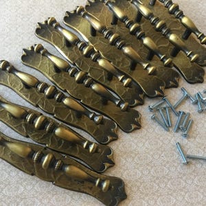 May include: A set of antique-style bronze cabinet pulls with matching screws. The pulls feature a decorative leaf design on the base and a detailed handle. These are ideal for adding a vintage touch to furniture.